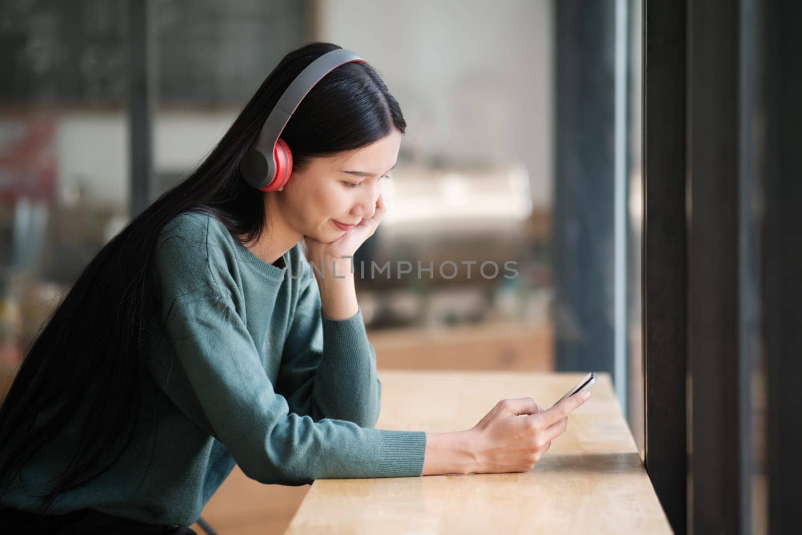 A woman wearing headphones is looking at her cell phone by ijeab