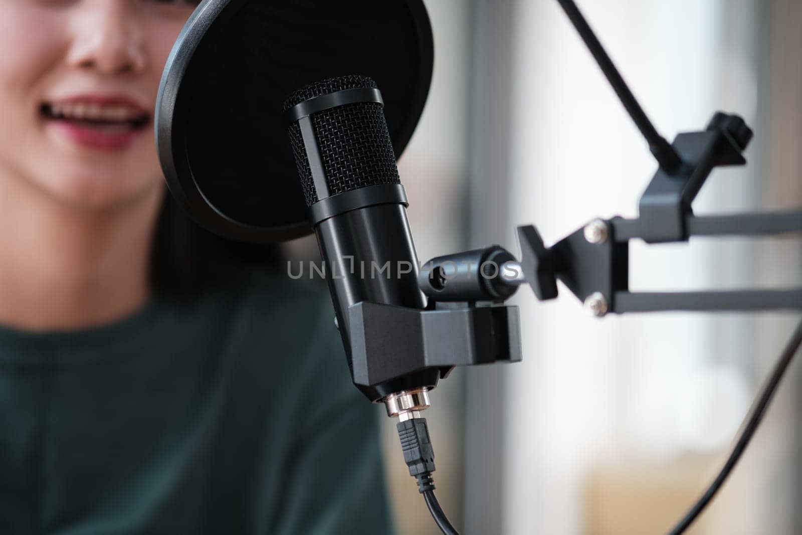 A woman is sitting in front of a microphone. She is smiling and she is happy. The microphone is black and has a black cord attached to it