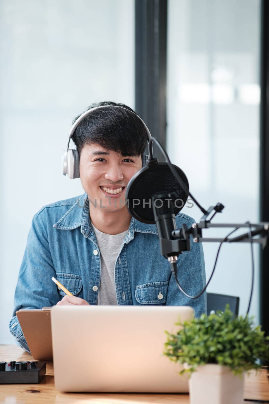 A man wearing headphones is sitting at a desk with a laptop and a plant. He is smiling and he is enjoying himself