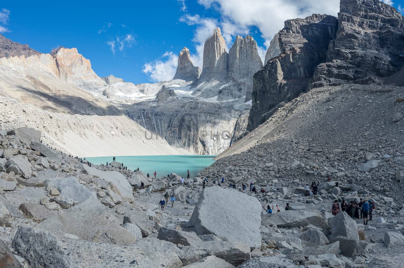 Travelers hike rugged paths to a breathtaking icy lake amid towering peaks.