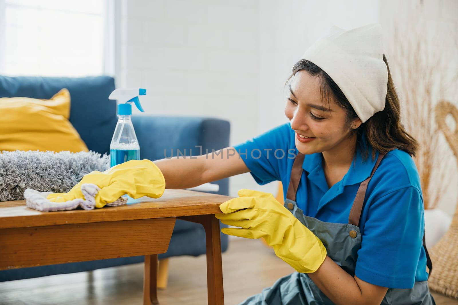 Engaged in housework a happy woman in yellow gloves wipes the table ensuring a clean living room. Her commitment to maintaining home hygiene and cleanliness is evident in her routine. maid clean desk.