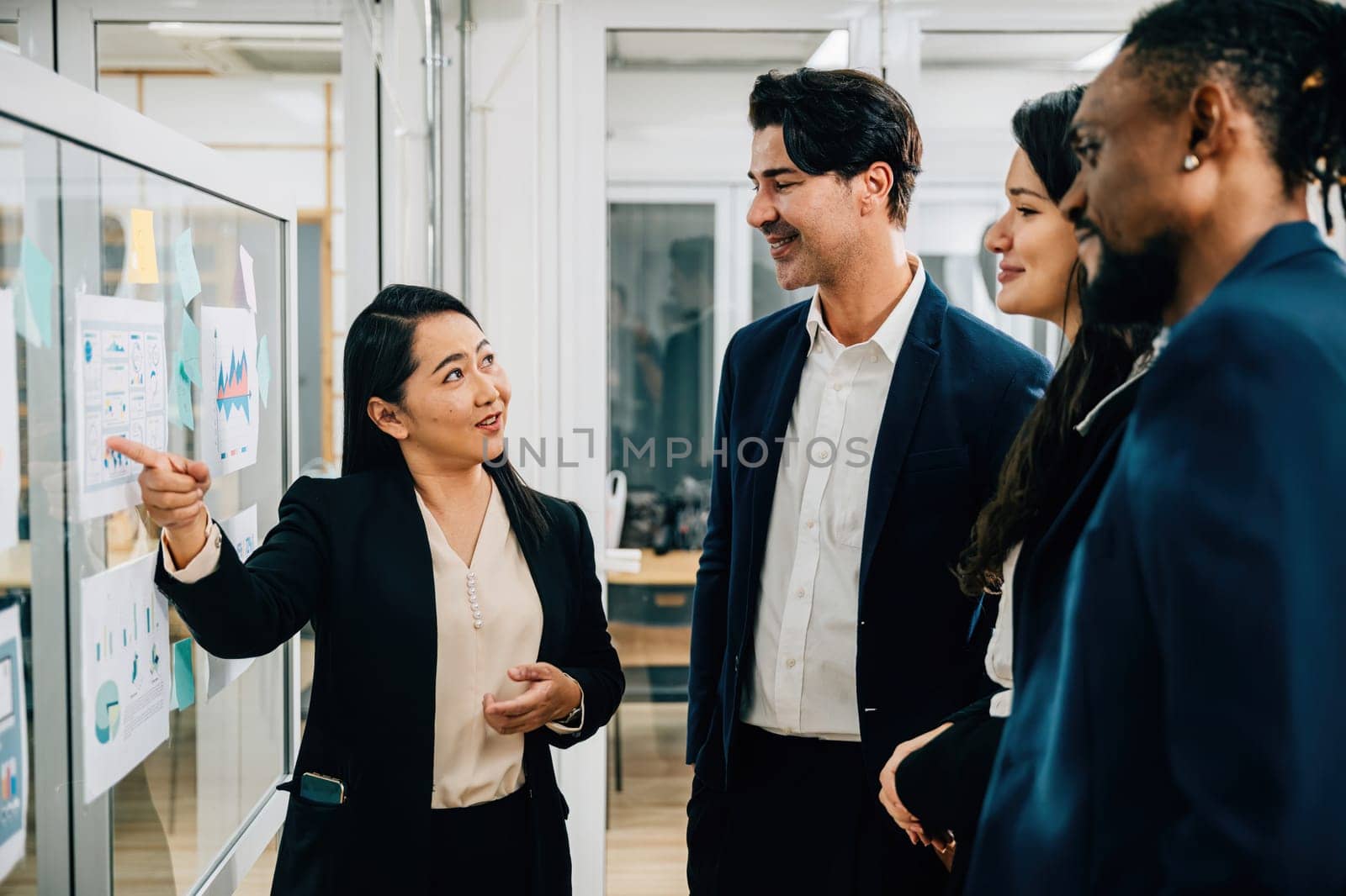 A diverse group of colleagues comes together for a meeting, actively discussing ideas and strategies around a whiteboard. Demonstrating effective teamwork, collaboration, and goal-oriented planning. by Sorapop