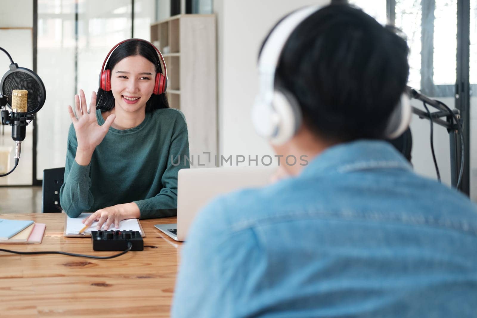 A woman wearing headphones is talking to someone on a laptop. The woman is smiling and waving at the person on the laptop