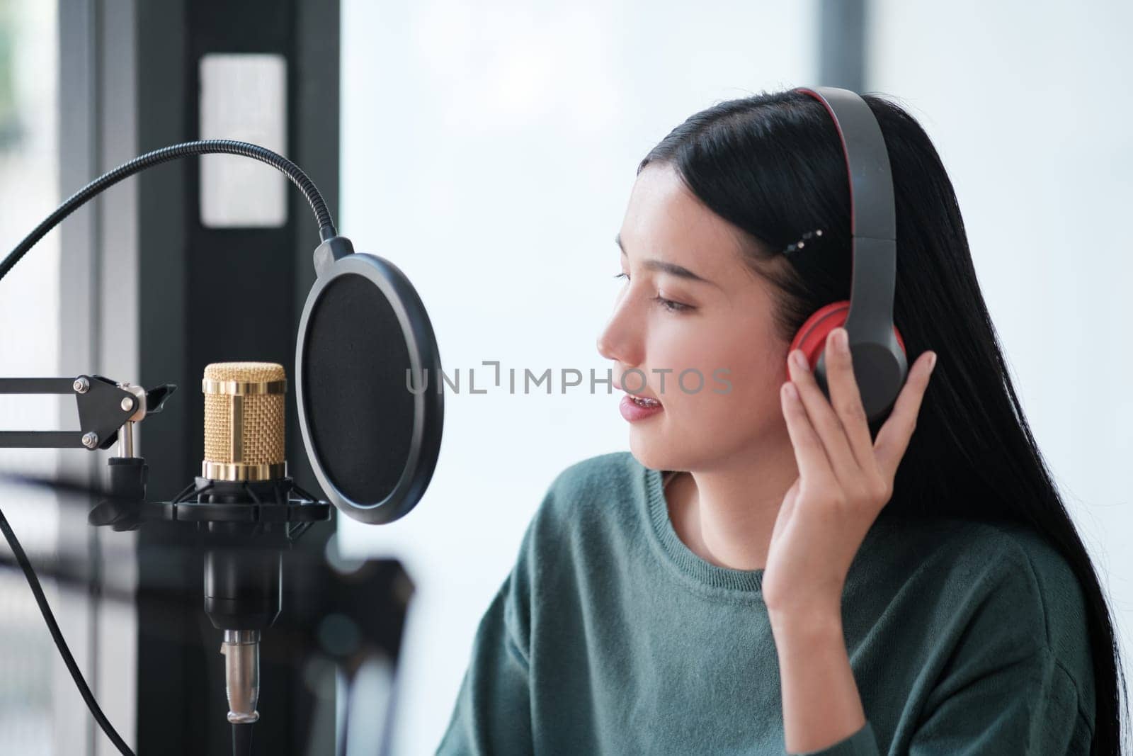 A woman is recording a song in a studio. She is wearing headphones and smiling. The studio is equipped with a microphone and a soundboard. The woman is enjoying the recording process