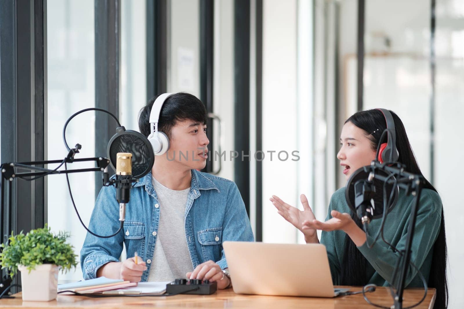 Two people are talking on a microphone. One of them is wearing headphones. The other person is looking at the camera