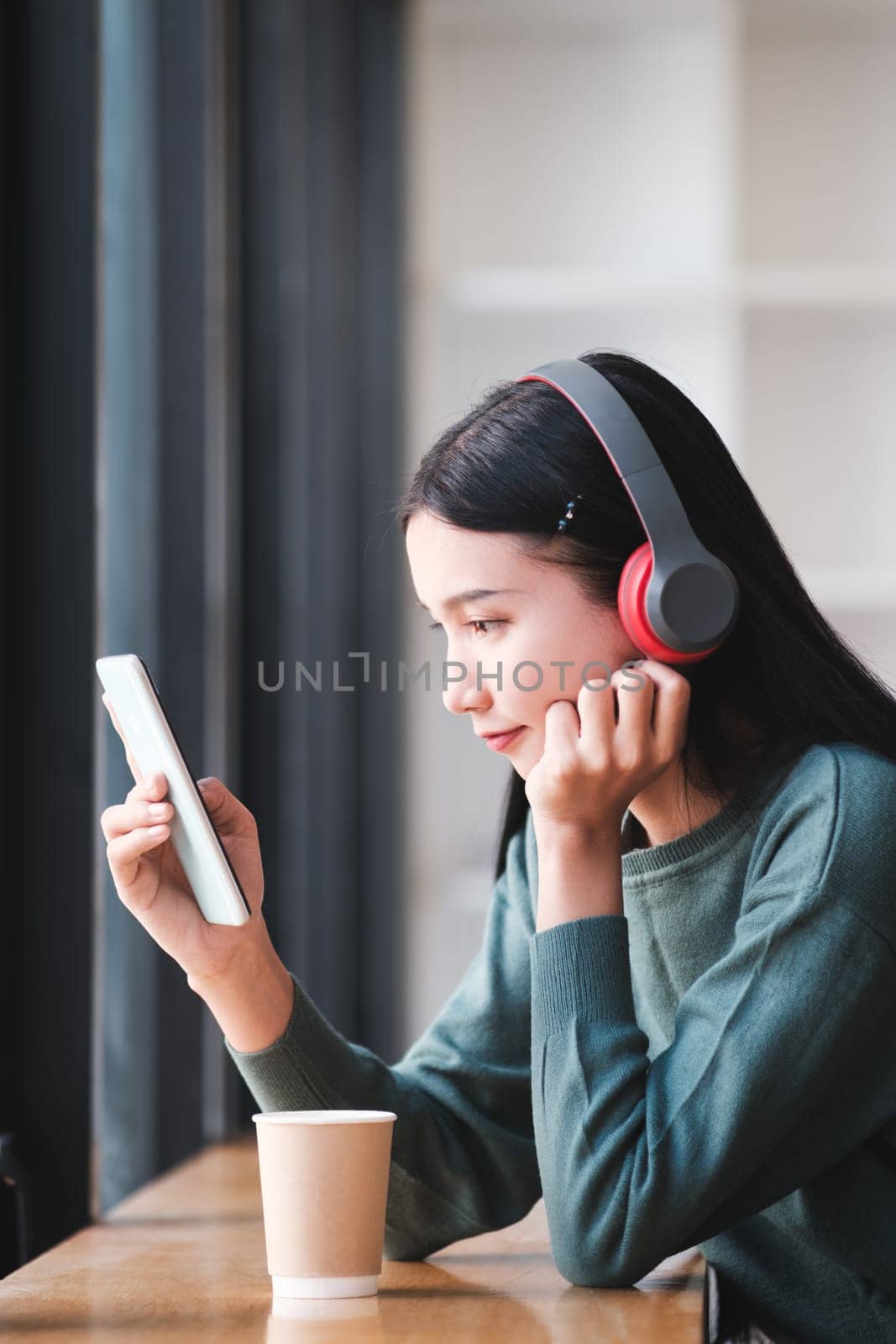 A woman is sitting at a table with a tablet and a cup of coffee. She is wearing headphones and looking at the tablet