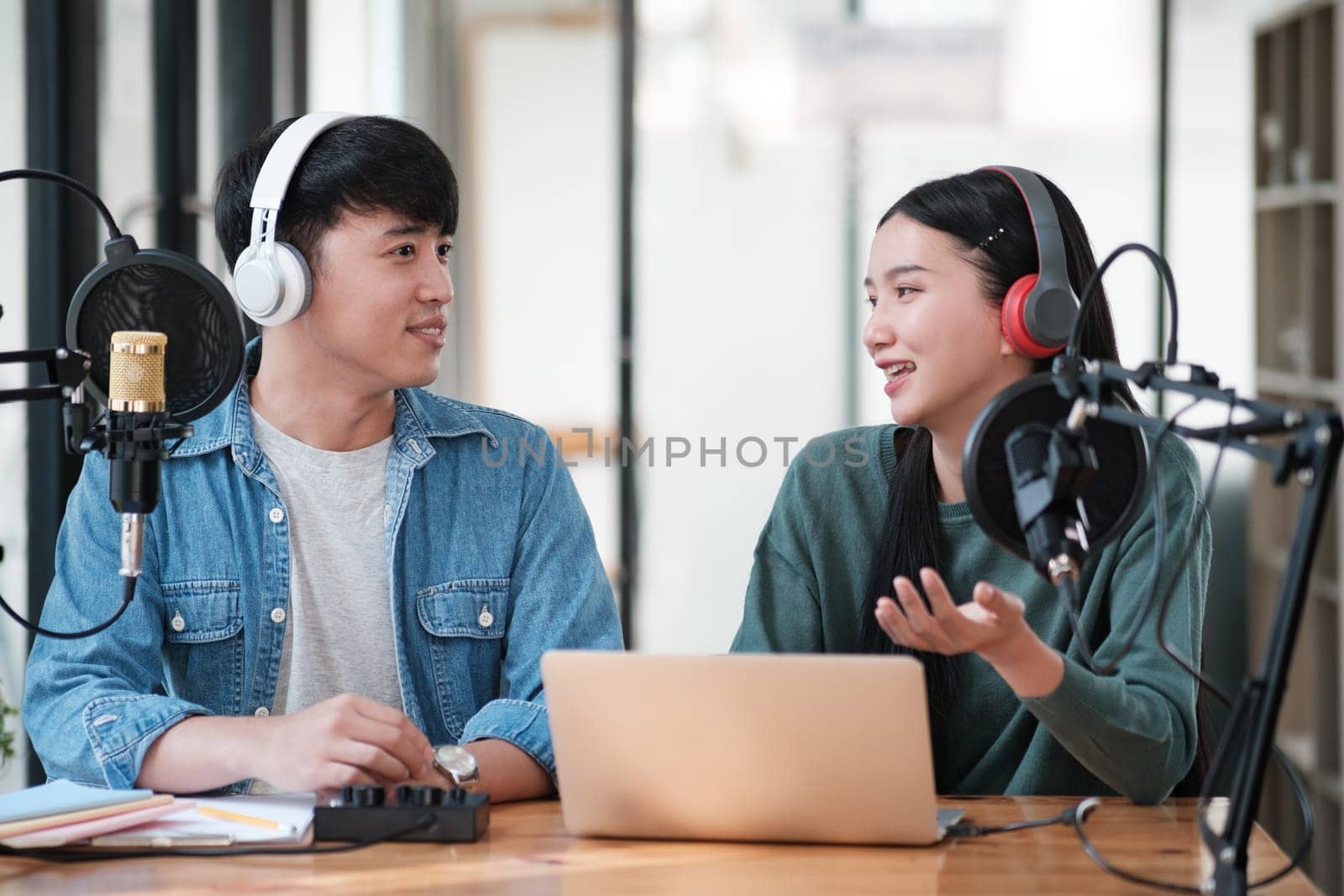 Two people are sitting at a desk with a laptop and microphones by ijeab