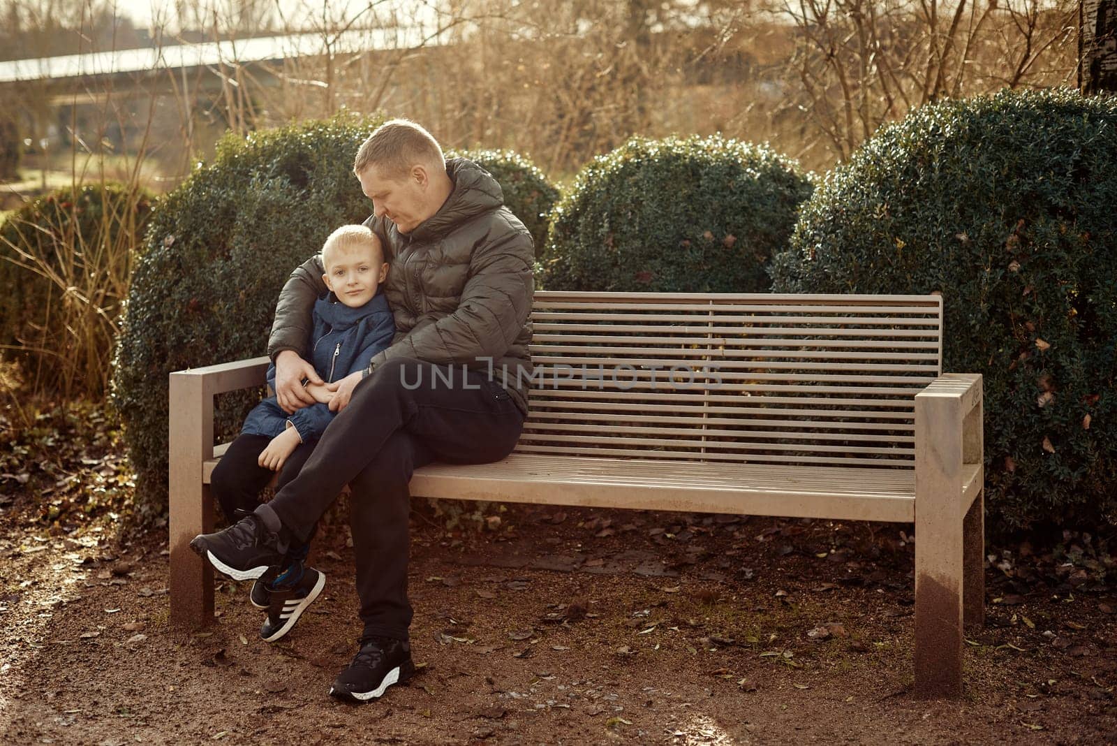 Autumnal Family Affection: Father, 40 Years Old, and Son - Beautiful 8-Year-Old Boy, Seated in the Park. Embrace the warmth of familial love in the autumnal air with this heartwarming image. A father, 40 years old, and his son - a beautiful 8-year-old boy, seated in the park. The essence of autumn adds a touch of seasonal charm to this delightful moment of family affection.