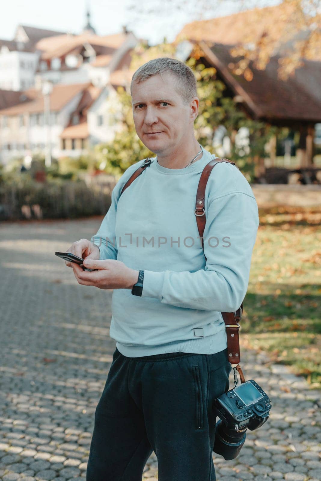 Professional Photographer Taking Picture Of Beautiful Autumn Park. Man Professional Photographer standing With Camera And With Smartphone In Autumn Park. Retouched, Vibrant Colors by Andrii_Ko