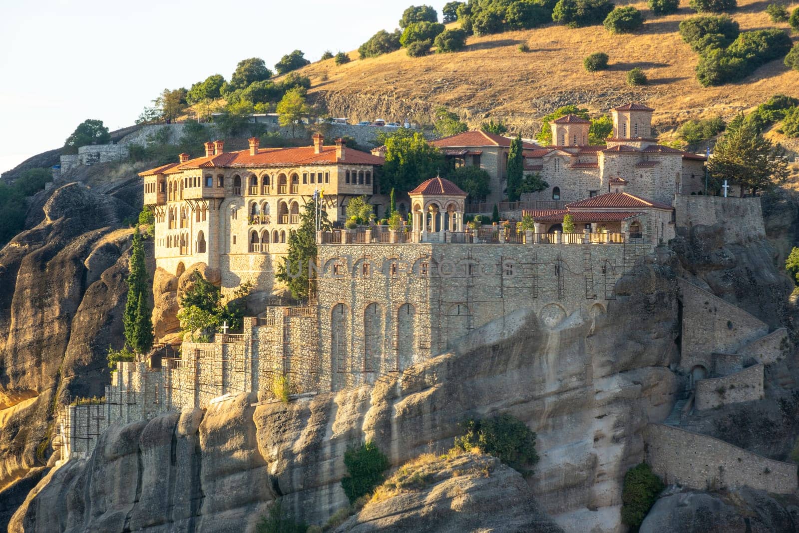 Greece. The end of a sunny summer day in Meteora. Large rock monastery near a green hill