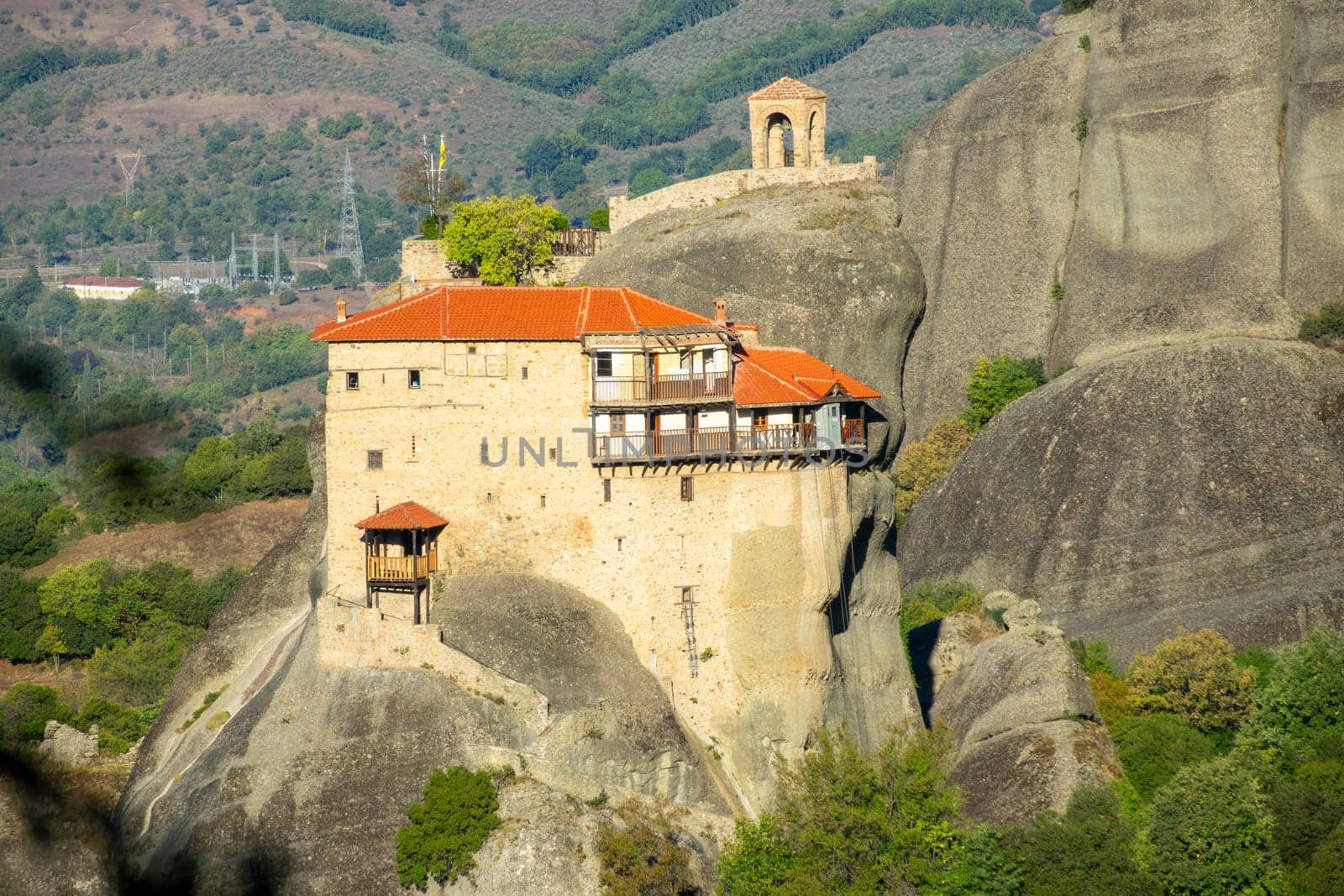 Greece. Sunny summer day in Kalambaka. A small monastery with red roofs on a cliff and a cable car