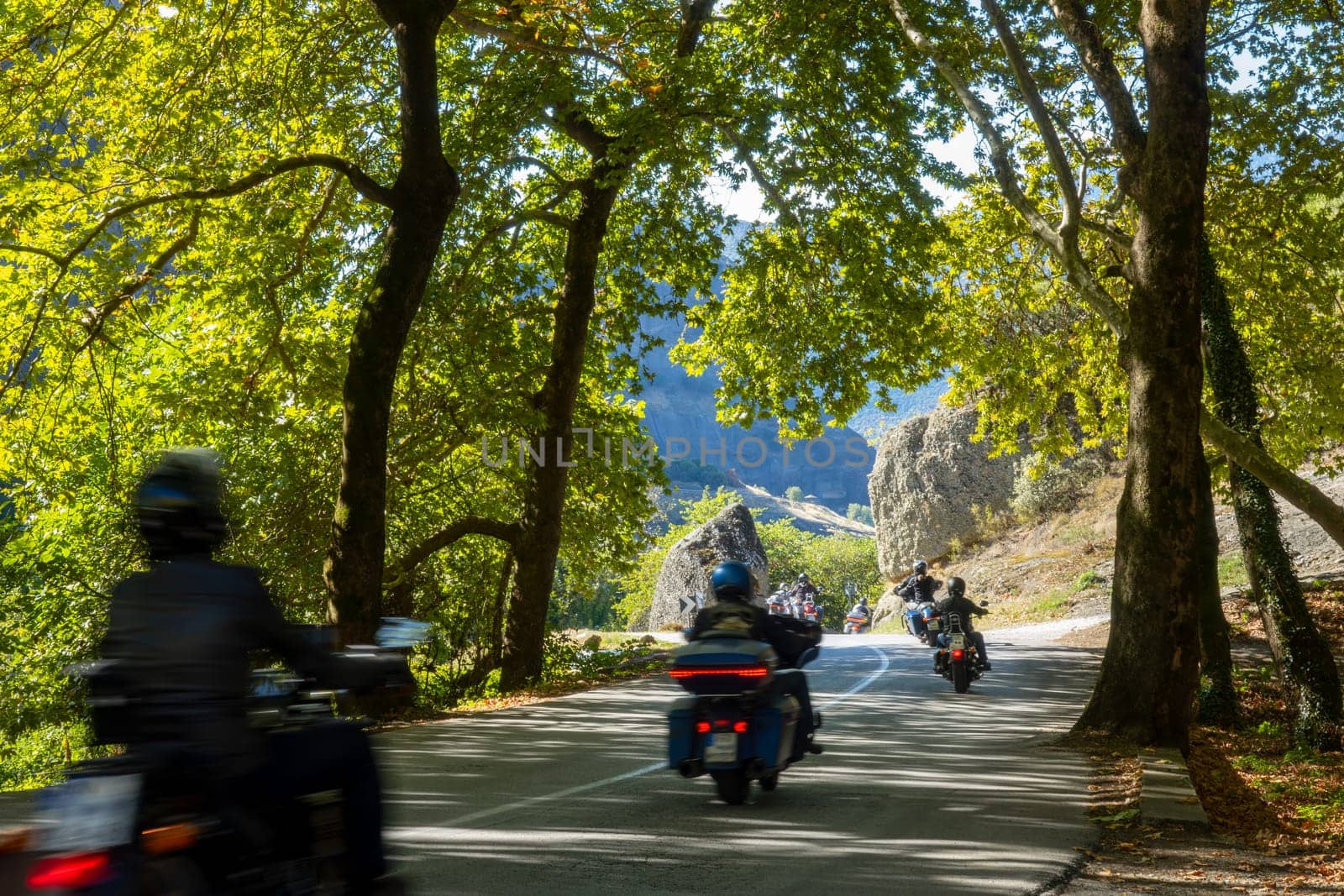 Greece. Summer sunny day in the shade of trees. Group of motorcycle tourists on a winding road