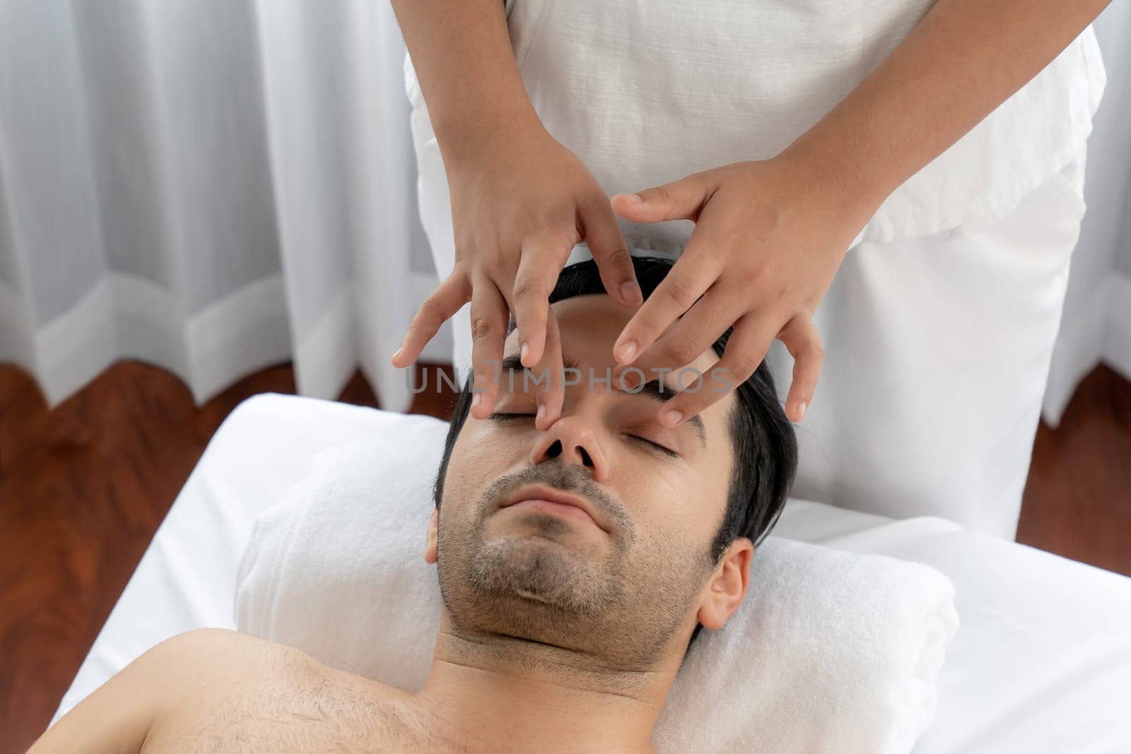 Caucasian man enjoying relaxing anti-stress head massage and pampering facial beauty skin recreation leisure in dayspa modern light ambient at luxury resort or hotel spa salon. Quiescent