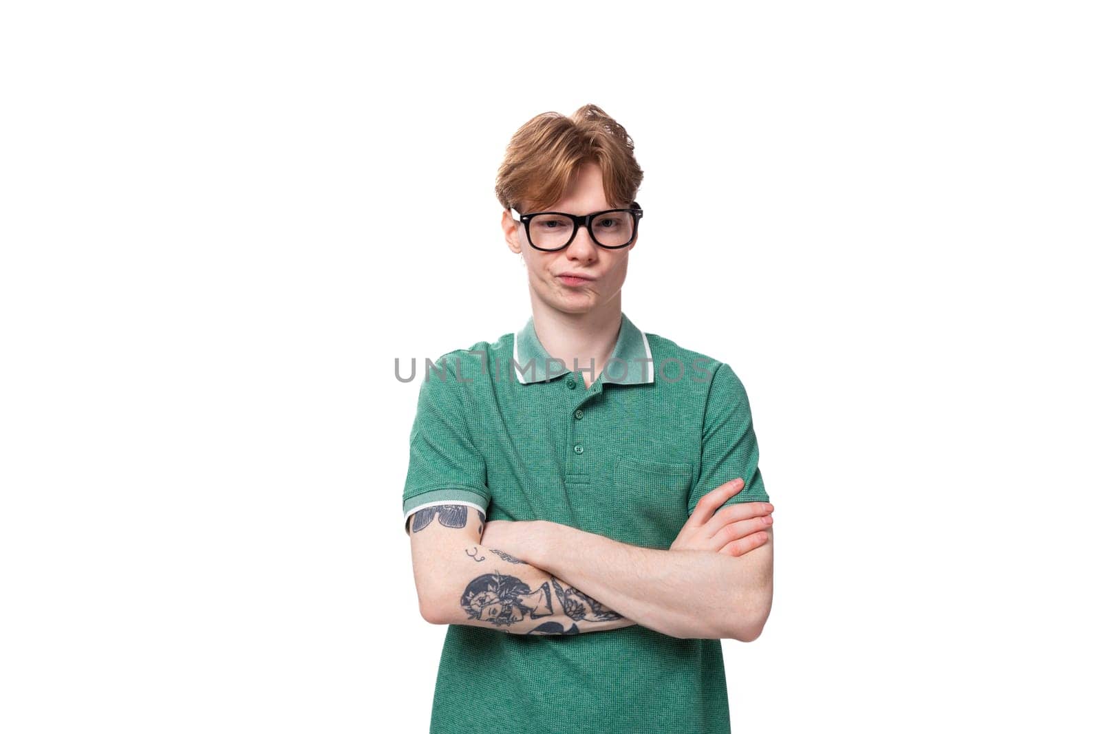 young red-haired man in a green t-shirt stands thoughtfully on a white background with copy space by TRMK