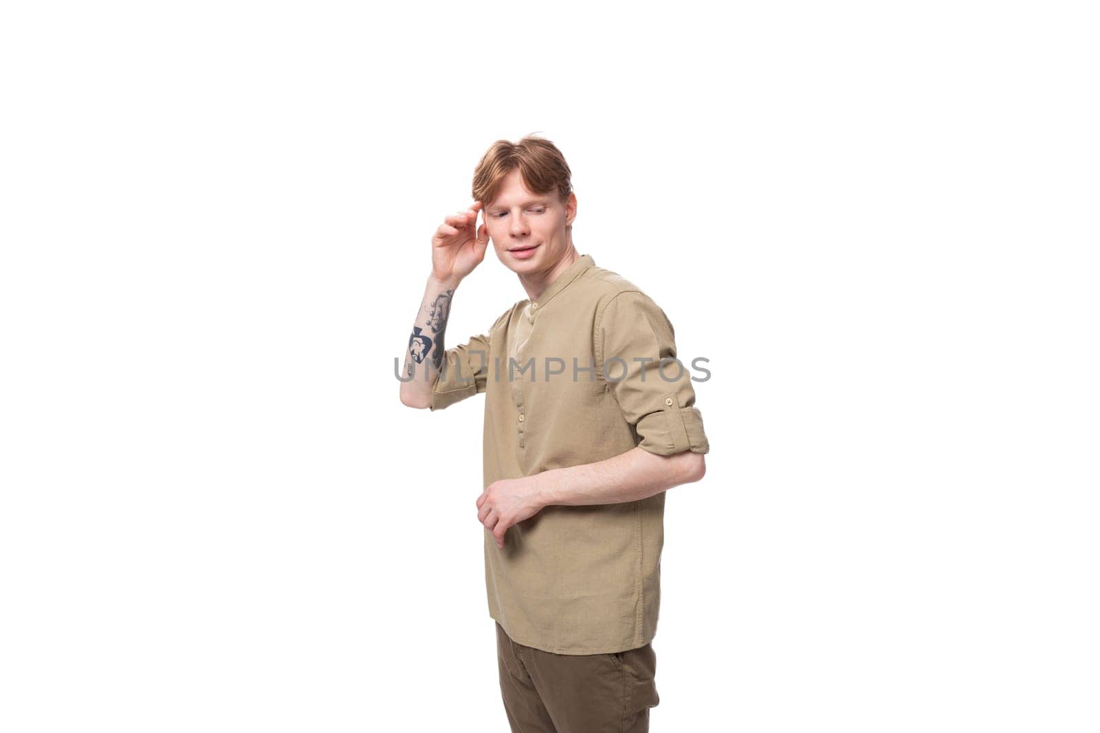 young well-groomed caucasian man with red hair is dressed in a khaki shirt and brown trousers on a white background by TRMK