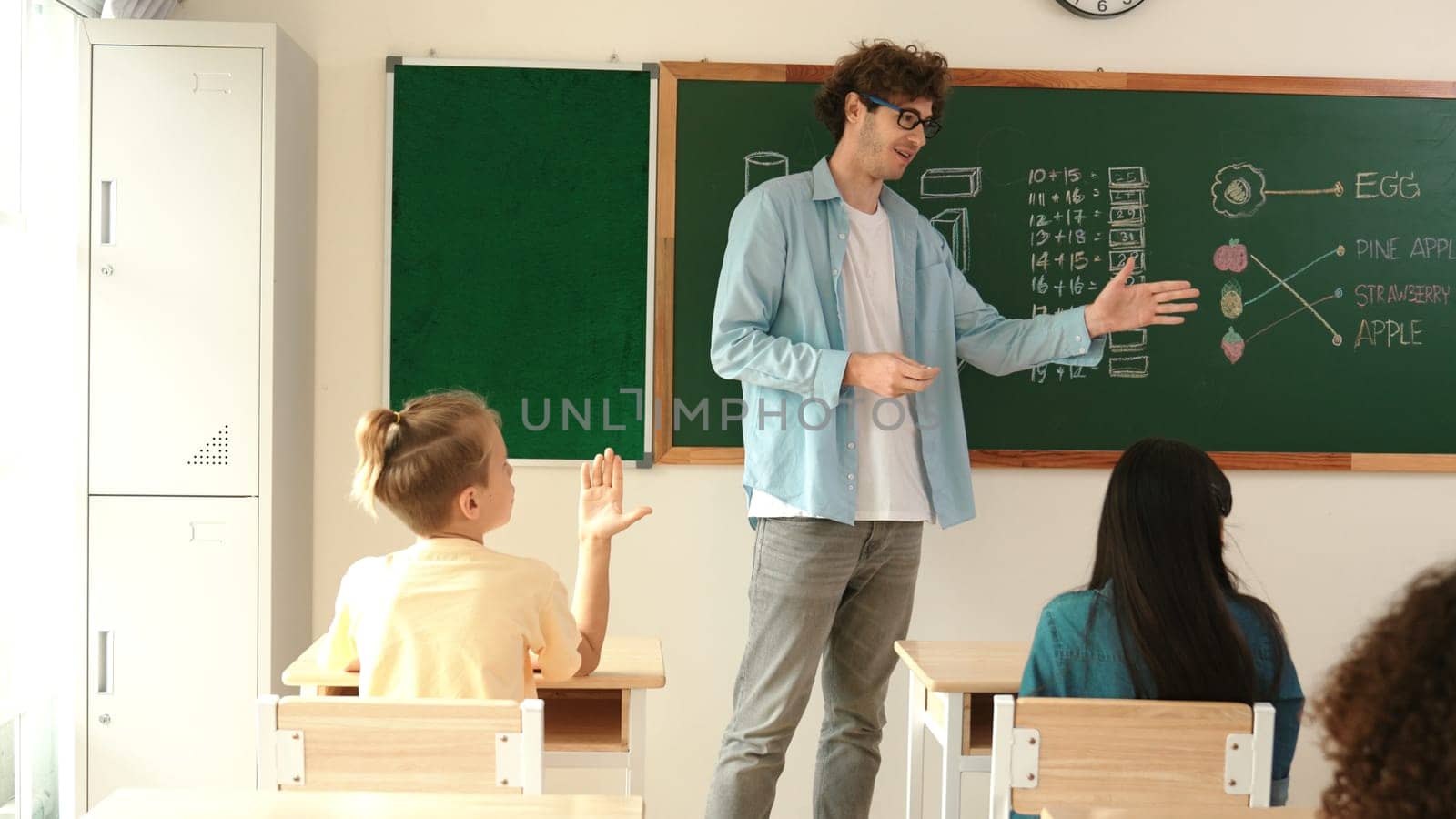 Caucasian teacher finding for volunteer to write answer on blackboard at math lesson. Teacher ask for volunteering to answer question while student receive chalk and walk in front of class. Pedagogy.