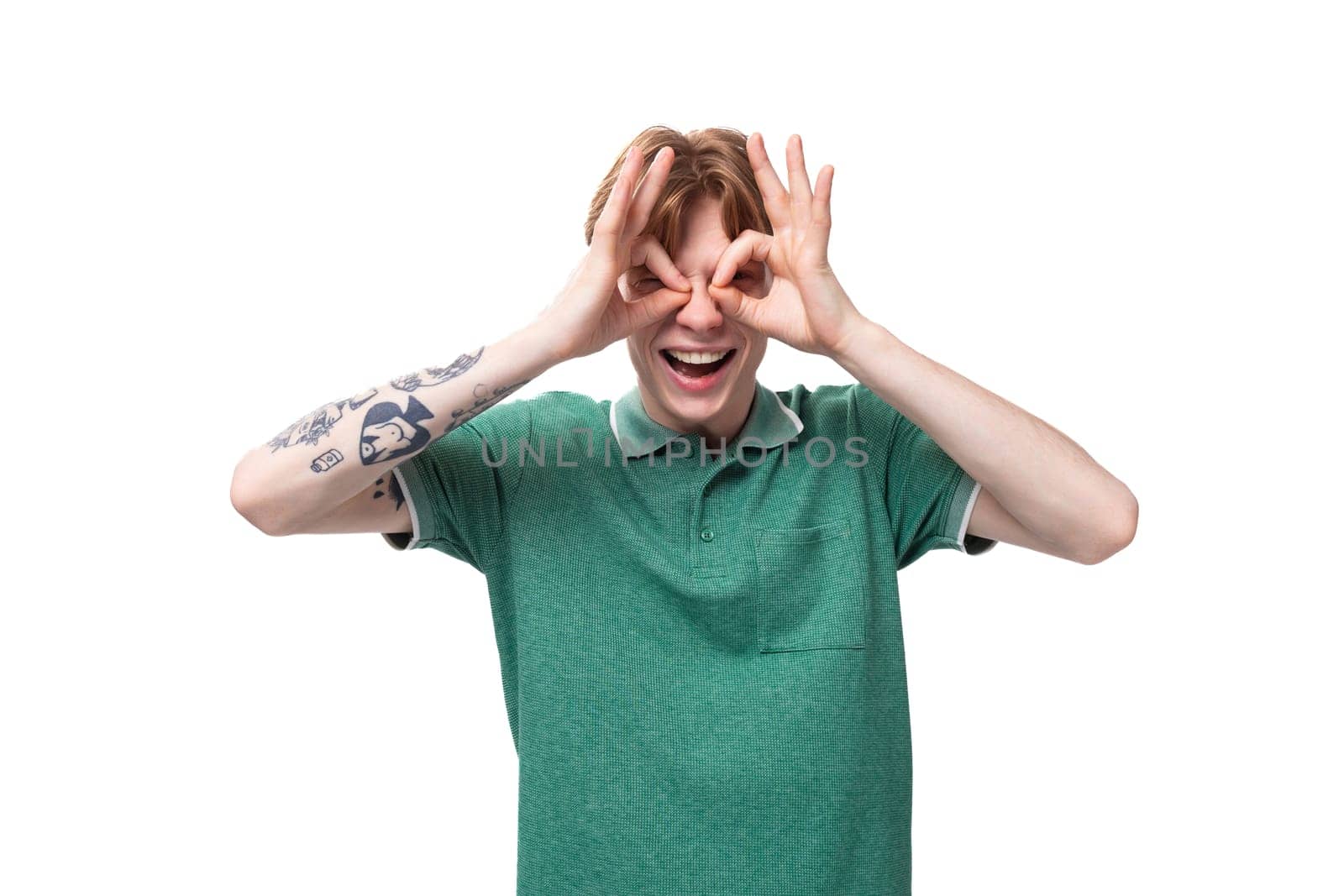 a young slender ginger man with a tattoo on his arm, dressed in a green T-shirt with bright facial expressions.