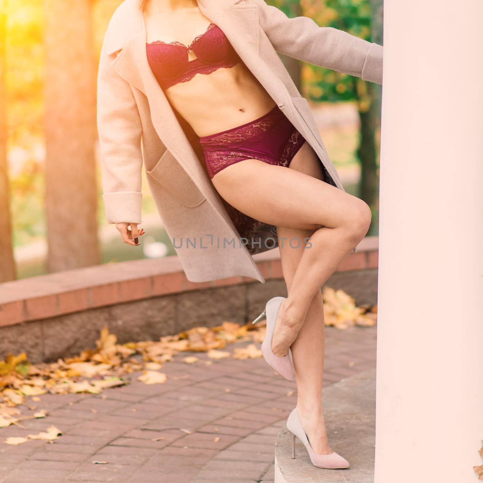 Young beautiful dark-haired woman with a slender figure posing in lingerie and a classic coat in an autumn park