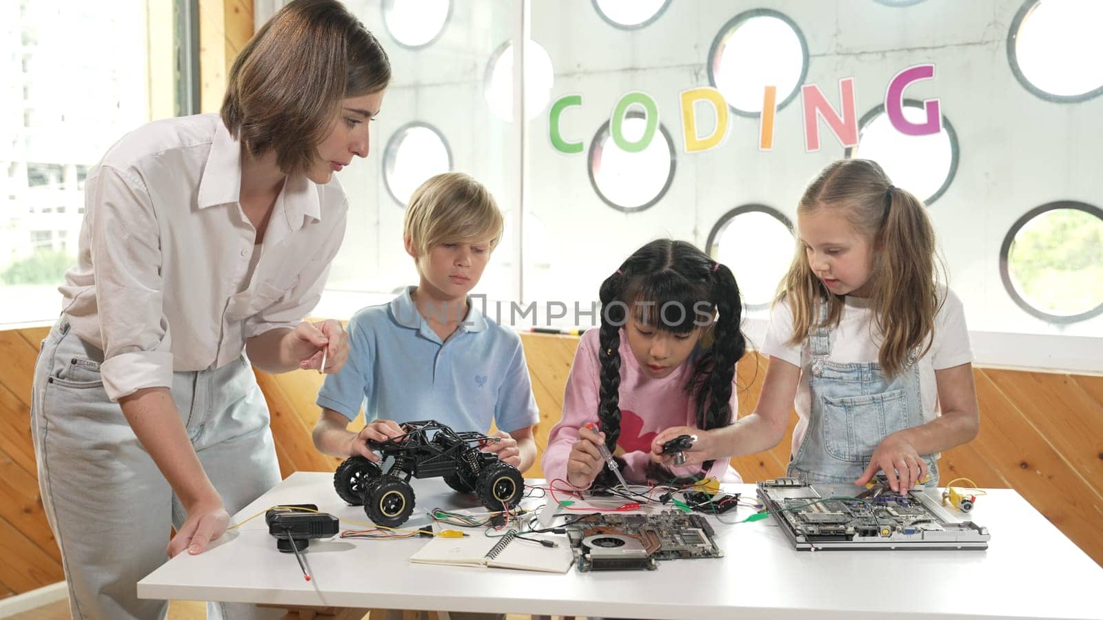 Young smart caucasian teacher teaching diverse students about electronic board. Multicultural children learn about digital electrical tool and fixing motherboard by using chips and wires. Erudition.