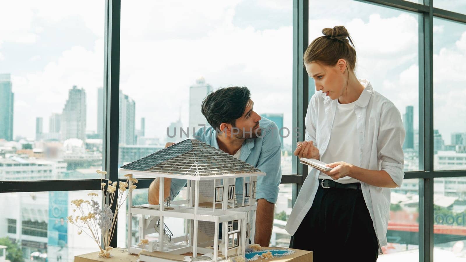 Skilled architect engineer team discussion about house model construction. Smart interior designer sharing, talking about building design while beautiful coworker taking a note. Design. Tracery