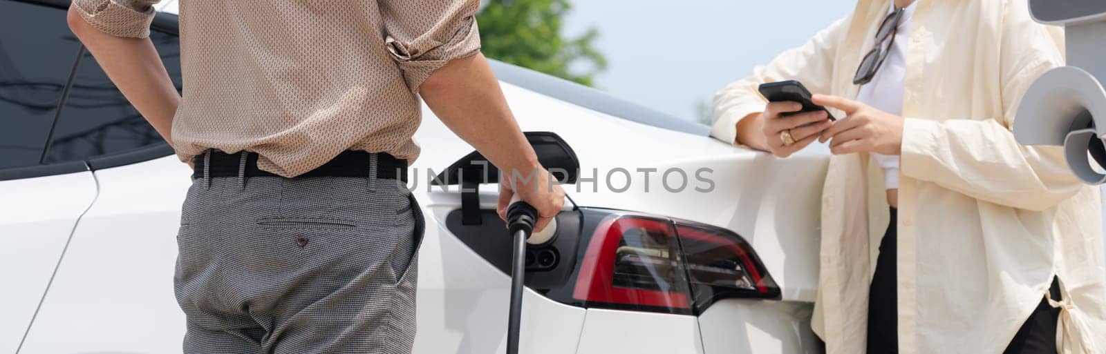 Young couple use smartphone to pay for electricity for EV car. Expedient by biancoblue