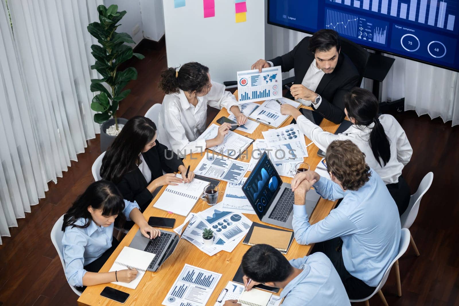 Wide top view of diverse group of business analyst team analyzing financial data report paper on meeting table. Chart and graph dashboard by business intelligence analysis. Meticulous