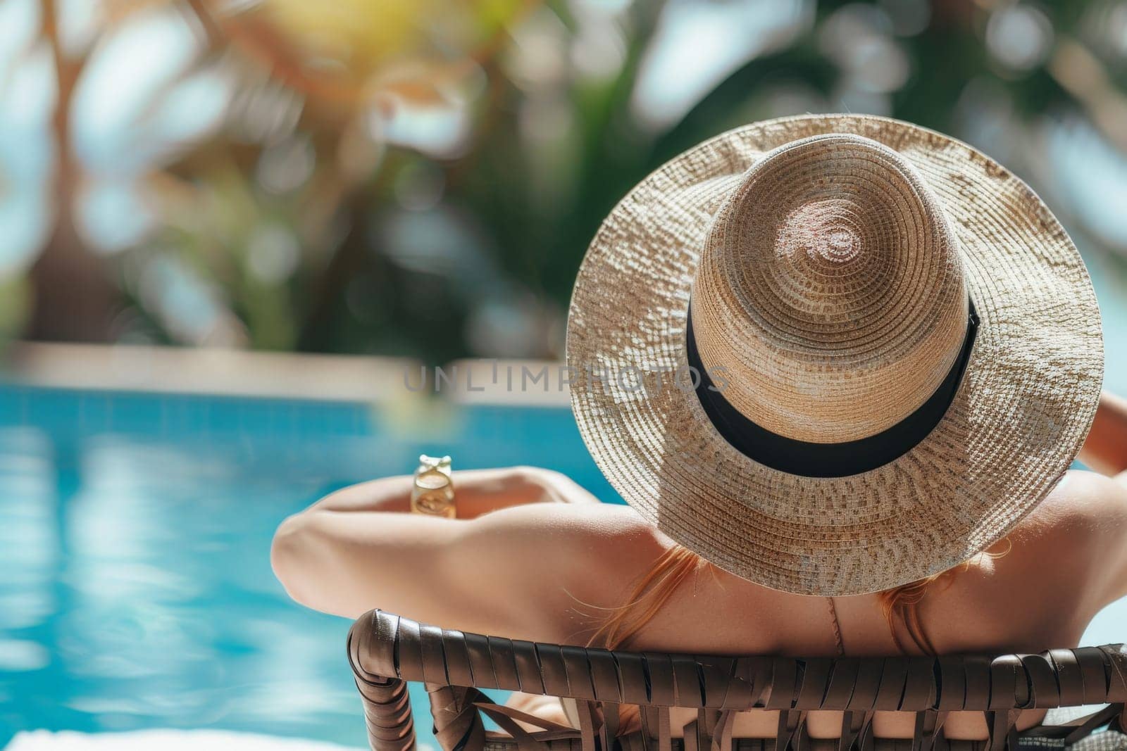 Fashionable woman in the back wearing a straw hat while on vacation at luxury poolside in resort.