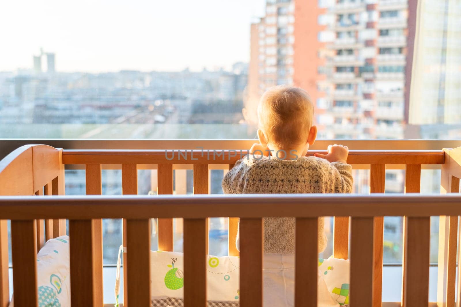 A child stands in front of the window and looks at the city from above.