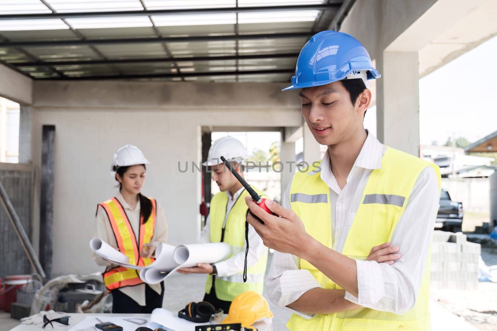 An electrical engineer stands with his arms crossed and holds a walkie-talkie while planning a construction project..