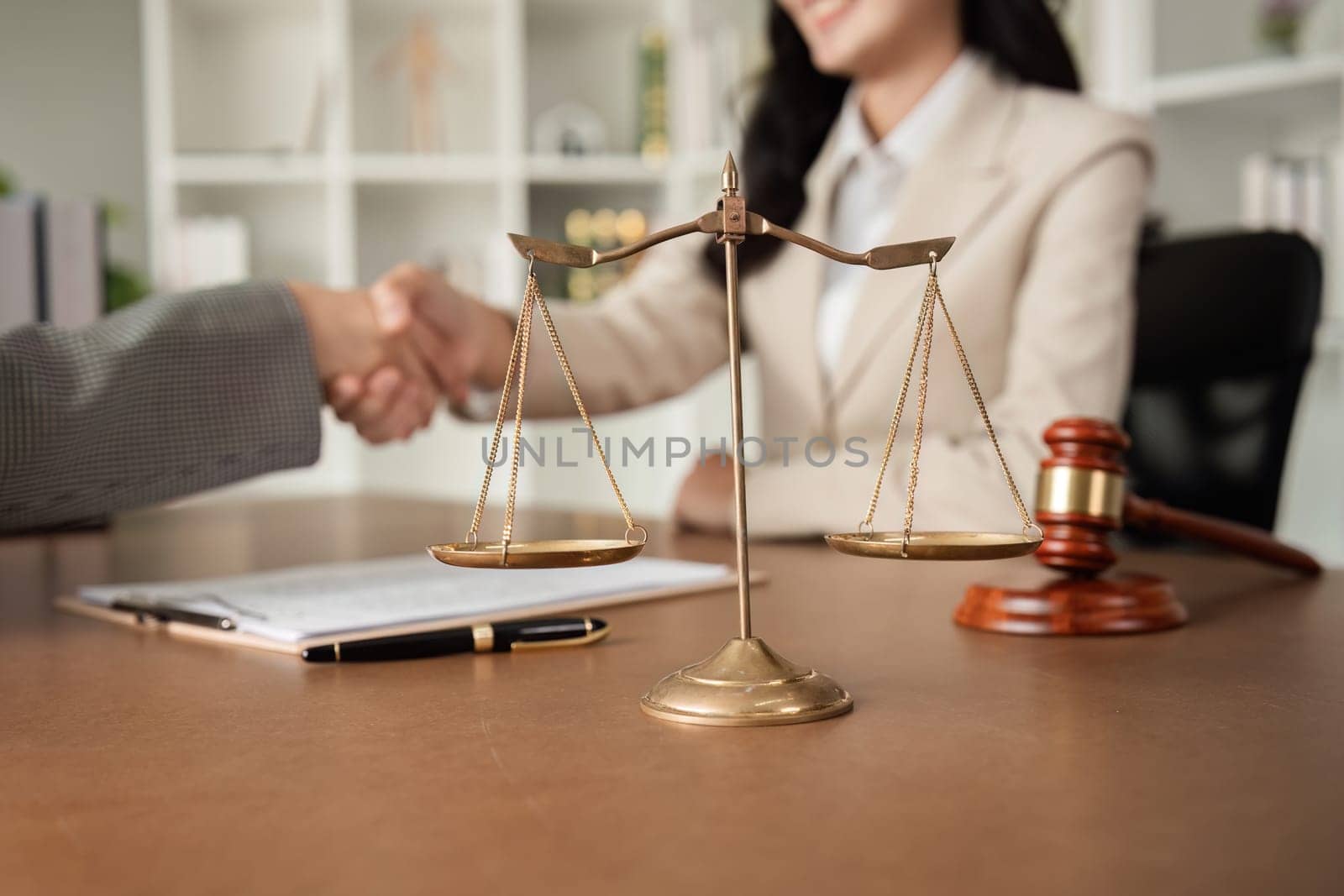 A lawyer and a businesswoman shake hands and reach an agreement on a cooperation contract document. In the lawyer's office and there is a hammer lying on the table..