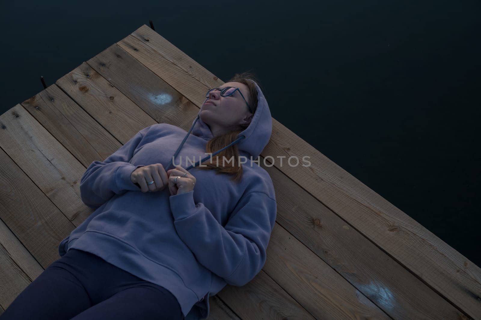 Woman lying down on the pier at lake, closeup portrait, summer sunset