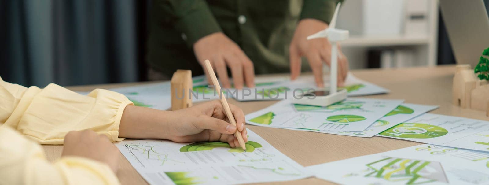 Professional businesswoman attended in green business meeting while male investor presenting about using clean energy on table with environmental document scatter around. Focus on hand. Delineation.