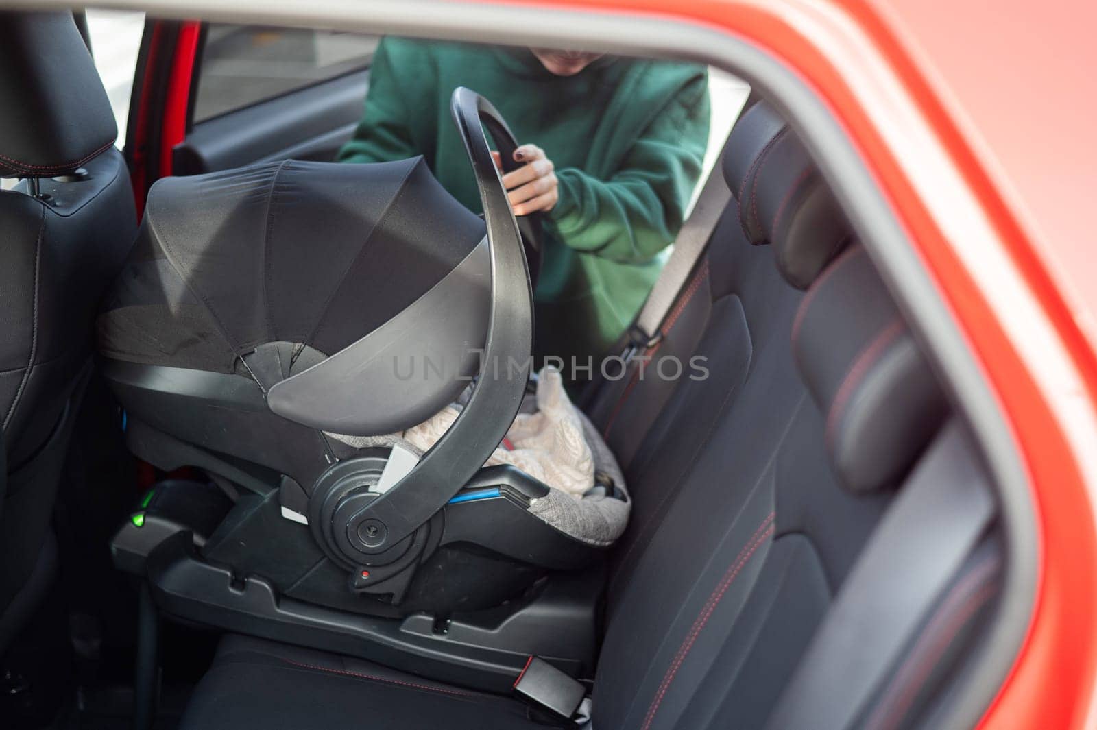 A Caucasian woman puts a child seat with a newborn baby in the car. Quick fastener