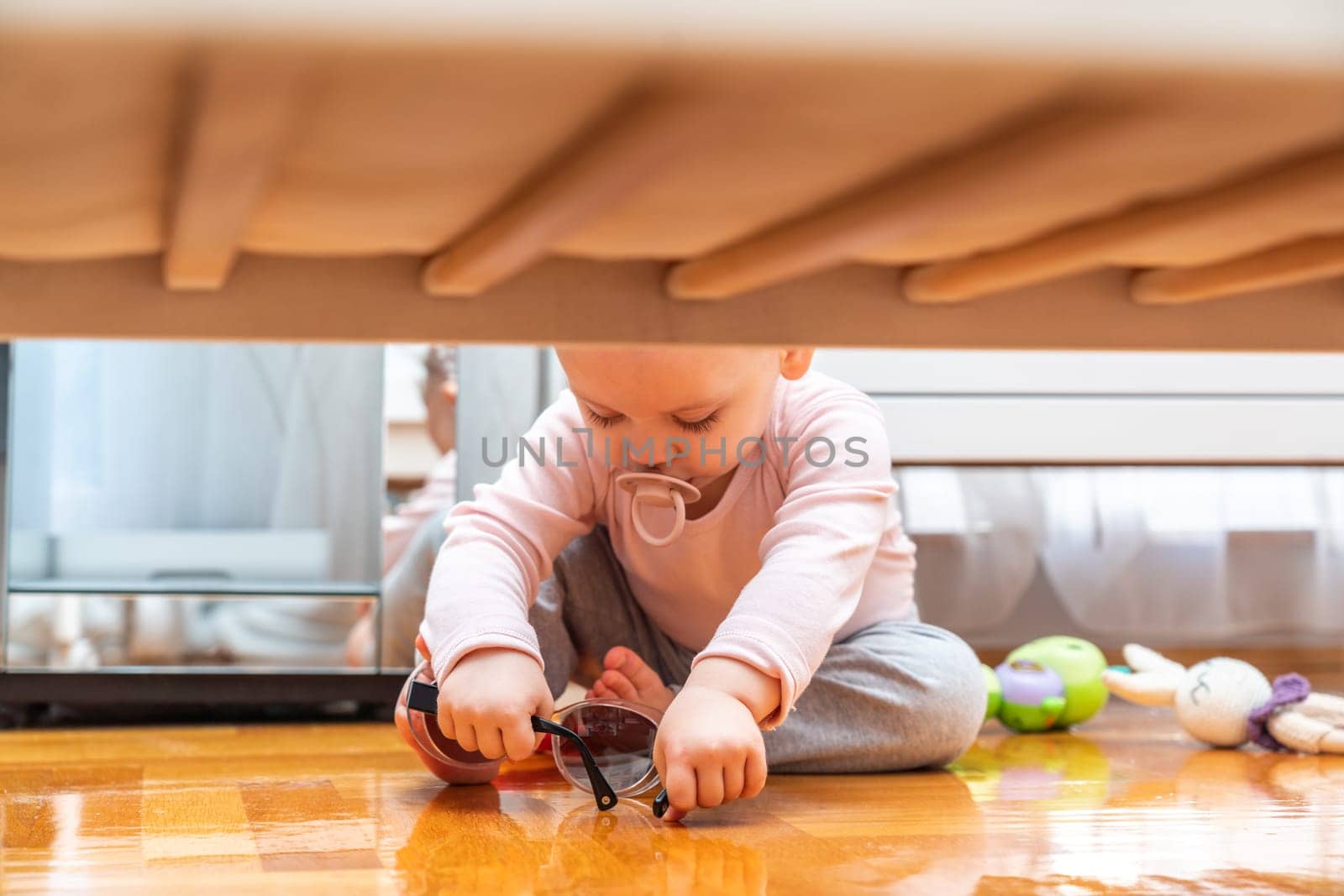 Baby with a pacifier in his mouth plays with toys, view from under the crib.