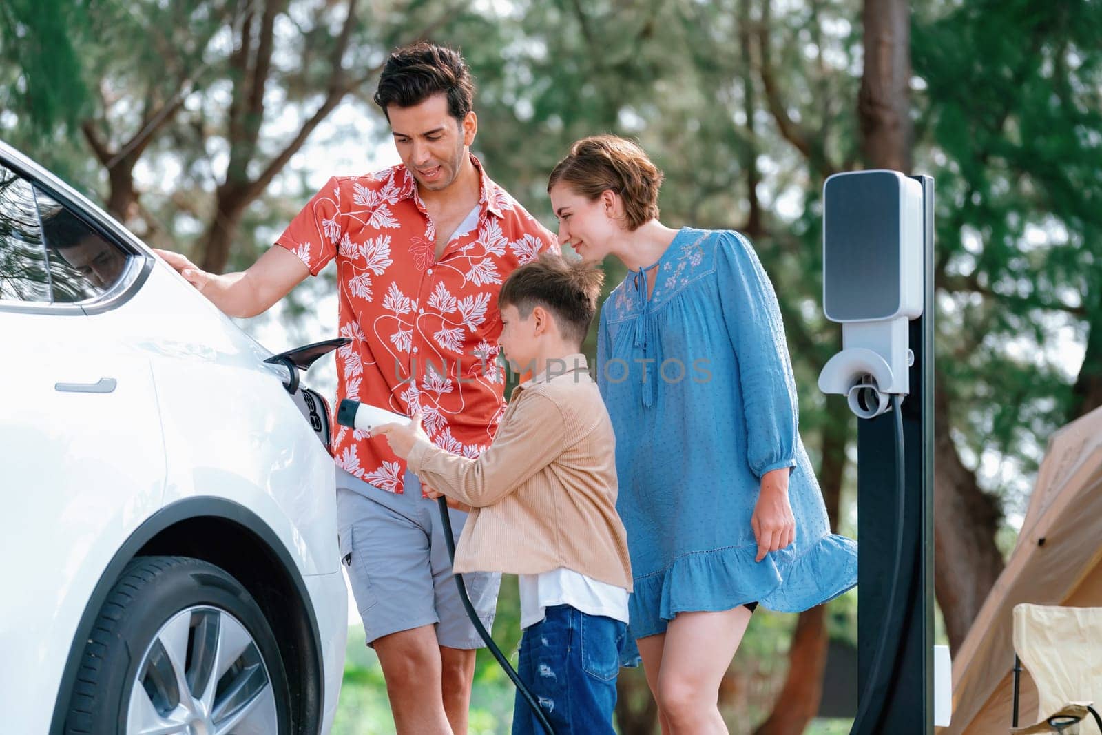 Outdoor adventure and family vacation camping in nature travel by eco friendly car for sustainable future. Lovely family recharge EV car with EV charging station in campsite. Perpetual