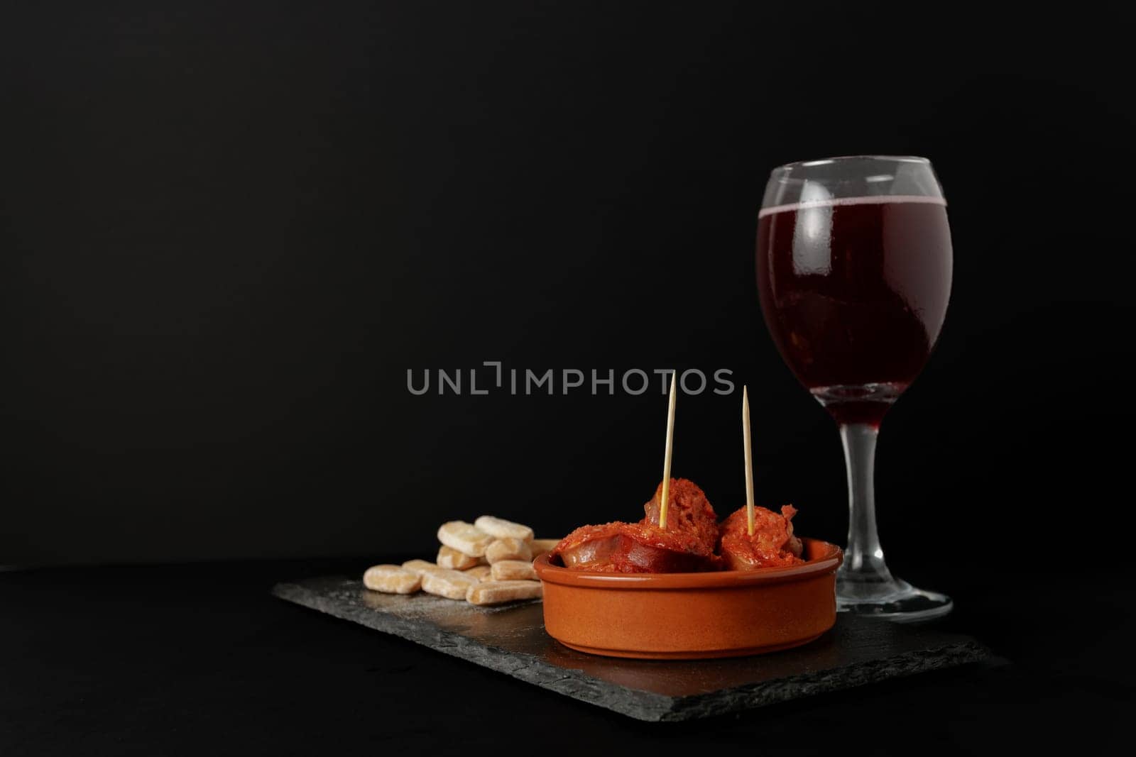 chorizo frito ,typical spanish tapa in a clay pot accompanied by bread and a glass of red wine.