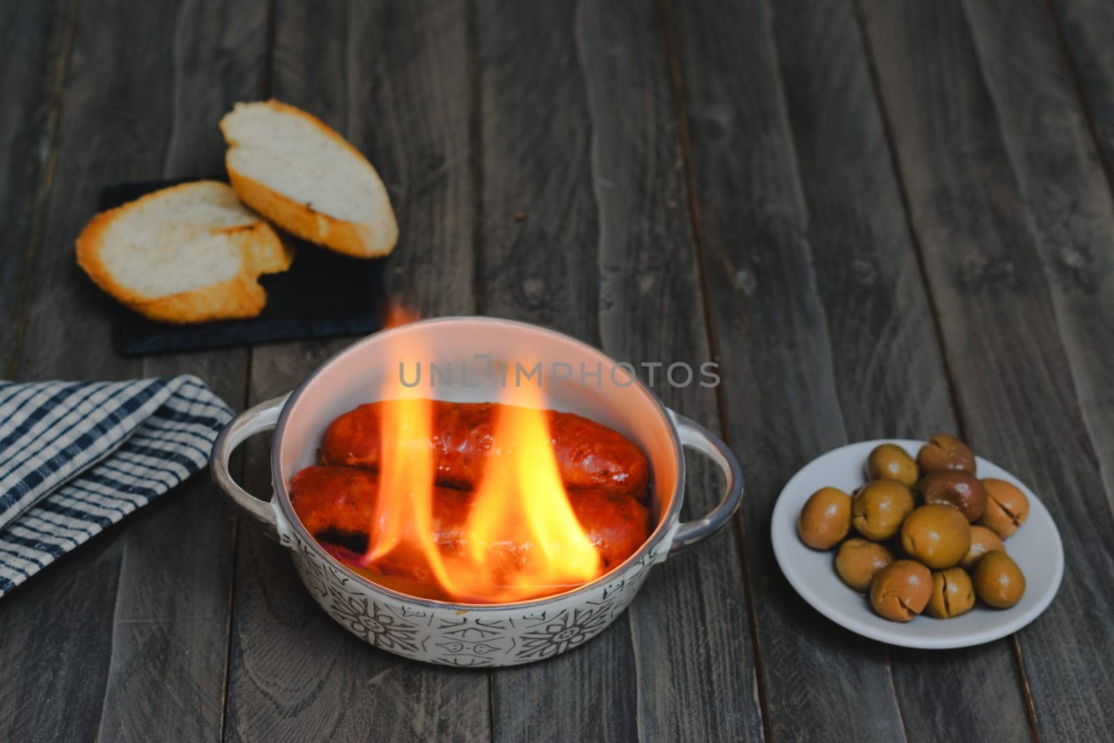 typical spanish tapa ,chorizo al infierno in ceramic casserole accompanied by bread and olives