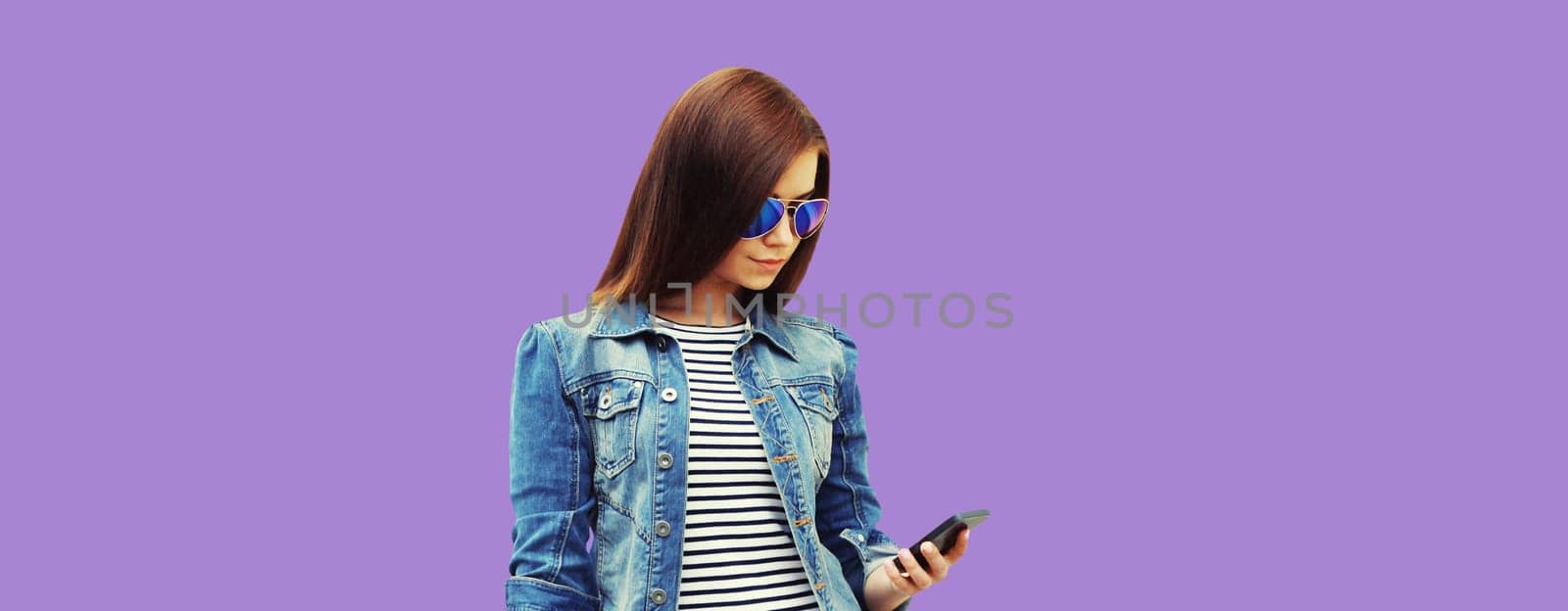 Modern stylish young woman with mobile phone on purple studio background