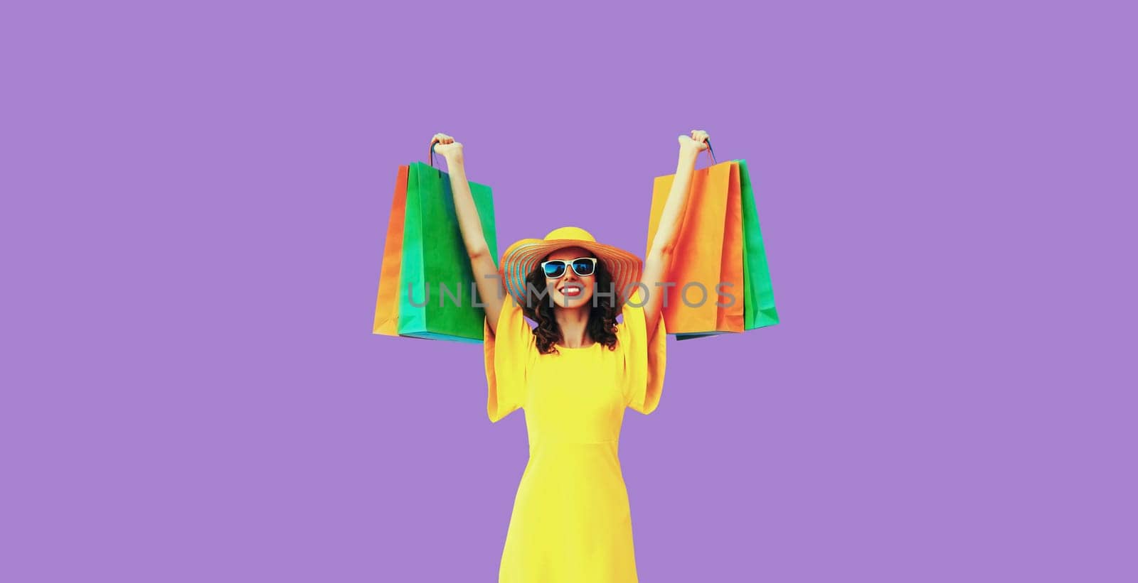 Stylish beautiful happy young woman model with shopping bags in summer straw hat on purple studio background