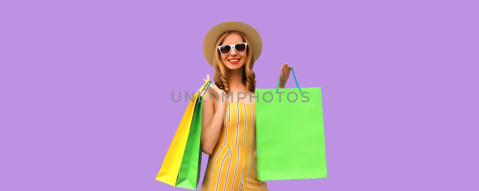 Stylish beautiful happy young woman model with shopping bags in summer straw hat on purple studio background