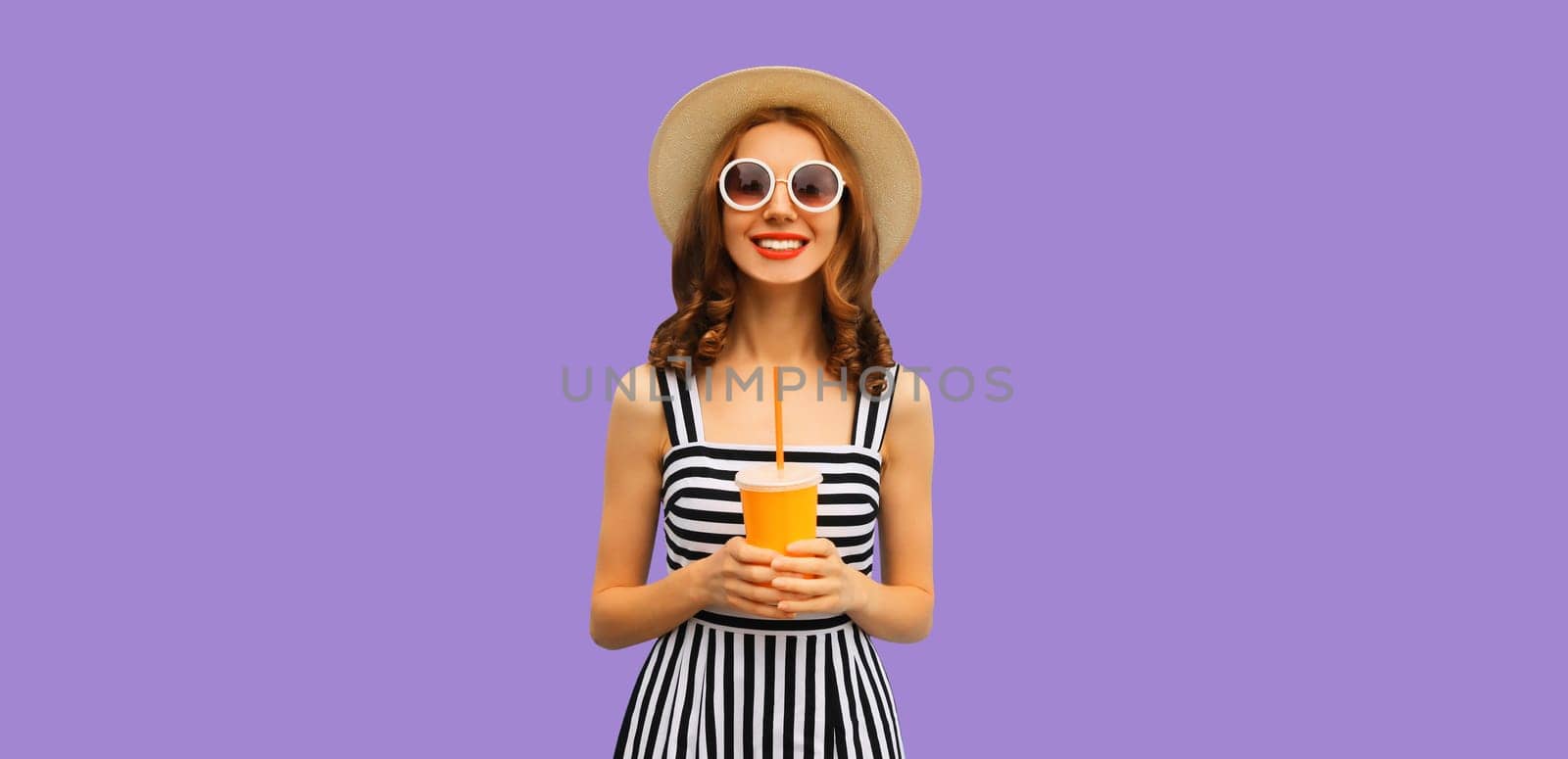 Summer portrait of happy smiling young woman with fresh juice in straw hat on purple studio background