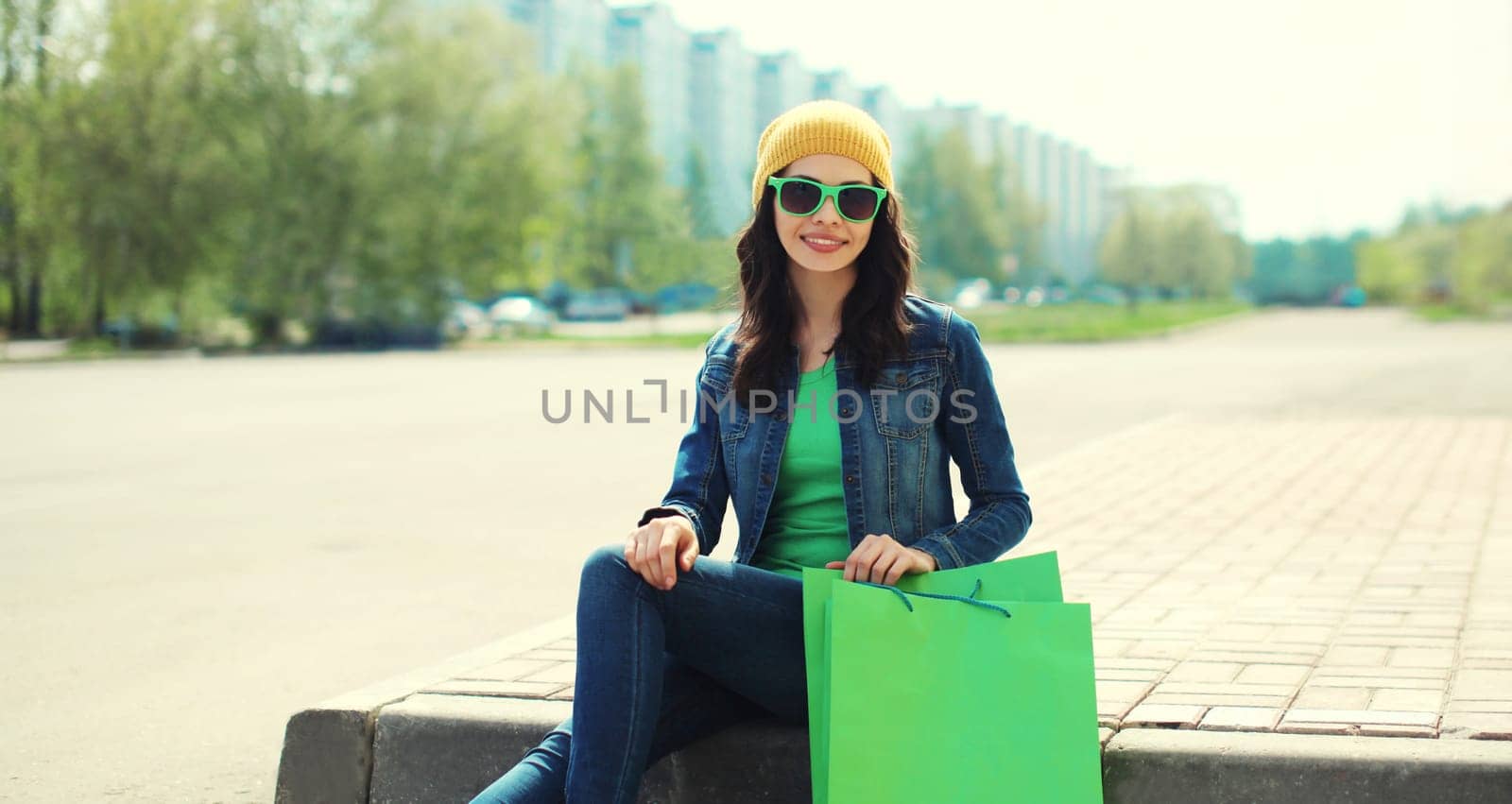 Portrait of happy brunette young woman with shopping bags sitting in the city
