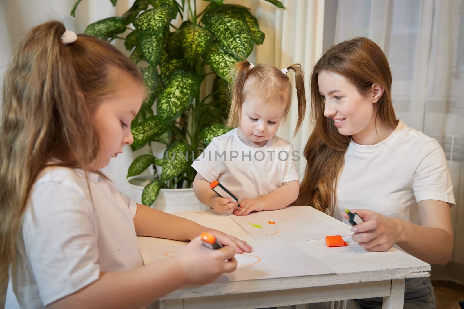 Young mother or babysitter, little daughter, sister teenager girl drawing at table in room. Painting, doing homework, family enjoying leisure at home by keleny
