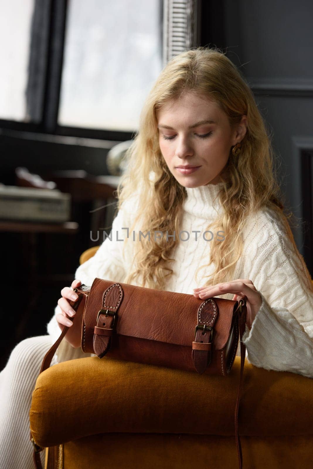 beautiful curly blond hair woman posing with a small tube brown bag in a vintage chair by Ashtray25