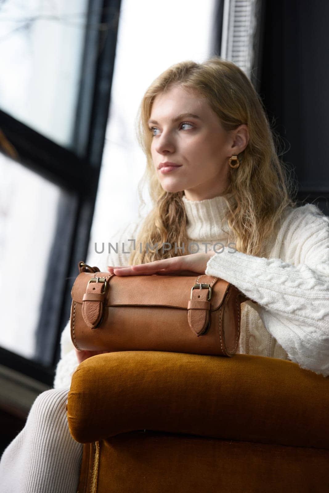 beautiful curly blond hair woman posing with a small tube brown bag in a vintage chair by Ashtray25