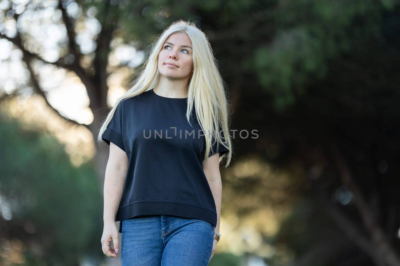 A young woman with blonde hair and braces is standing in a park, smiling.