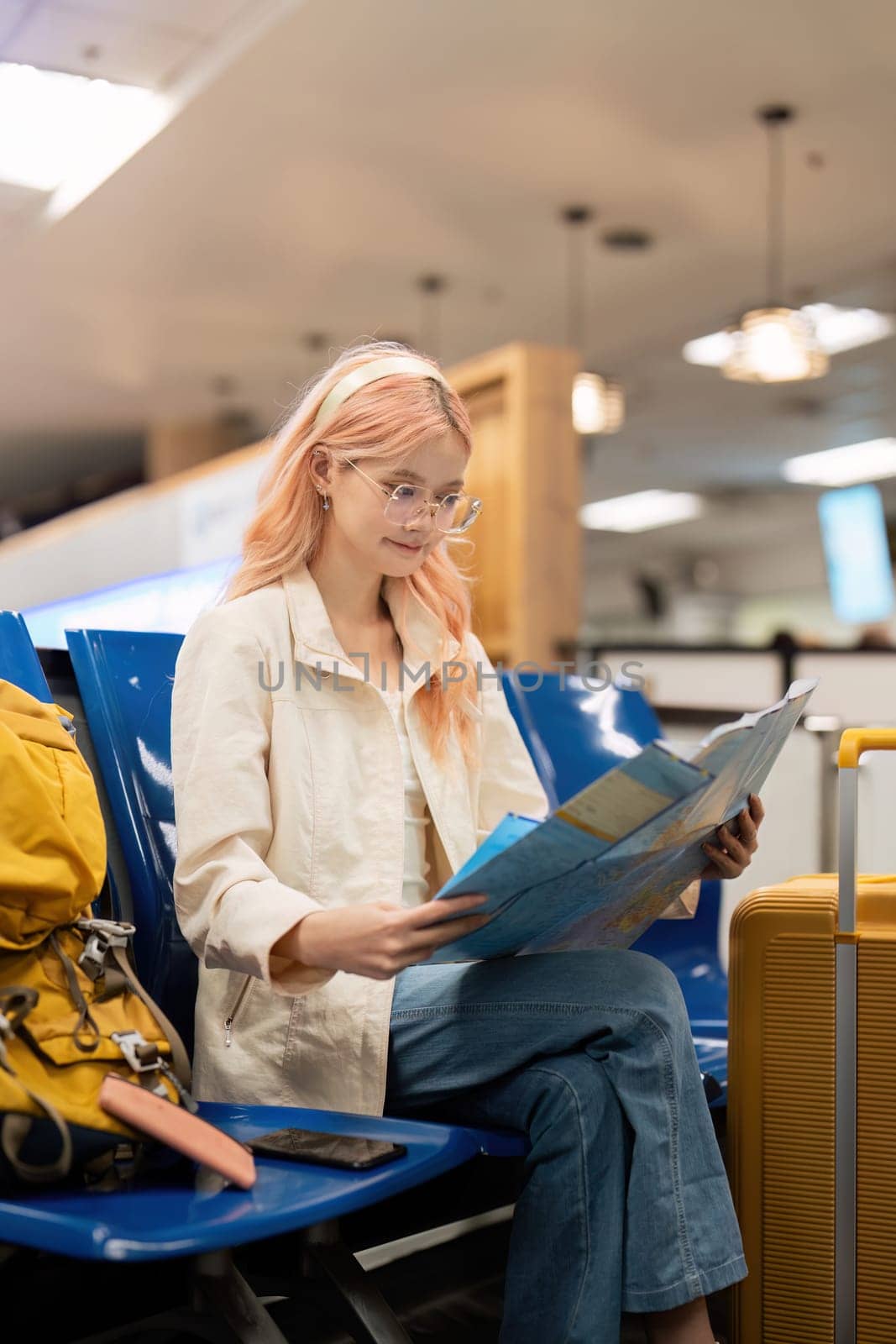 Happy young woman asian is sitting in airport near suitcase and reading map by nateemee