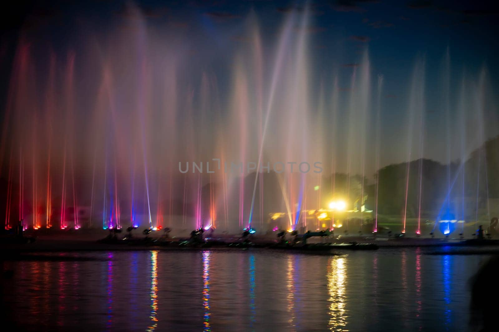 wide shot showing colorfully lit musical fountains public attraction on the famous tourist landmark Gadisar lake in Jaisalmer, Jodhpur Rajasthan with boats moving by Shalinimathur