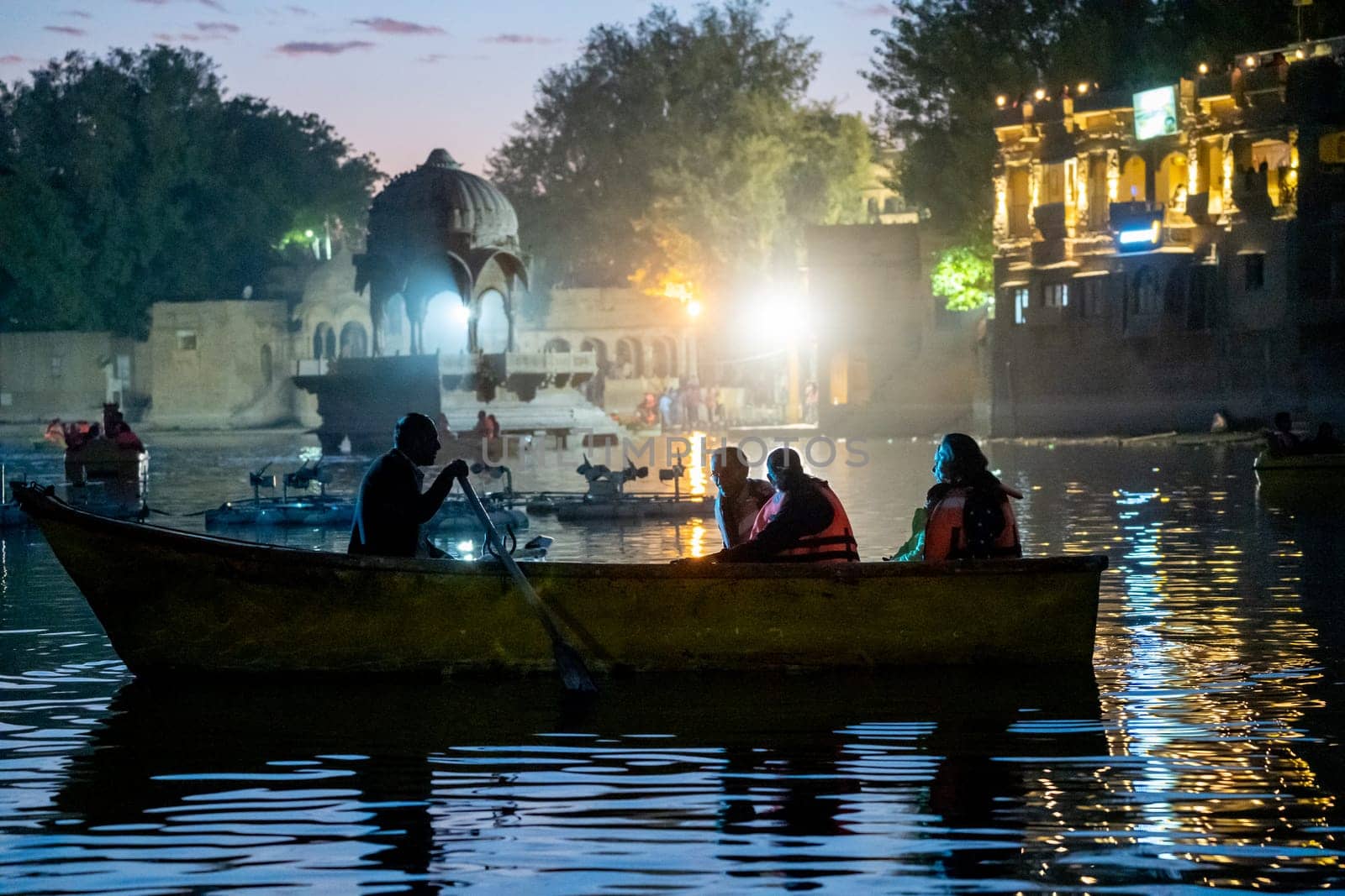 Family enjoying a night boat ride on the lit waters of Gadisar lake in Jaisalmer Jodhpur with the scenic palace and domes nearby a popular tourist destination India