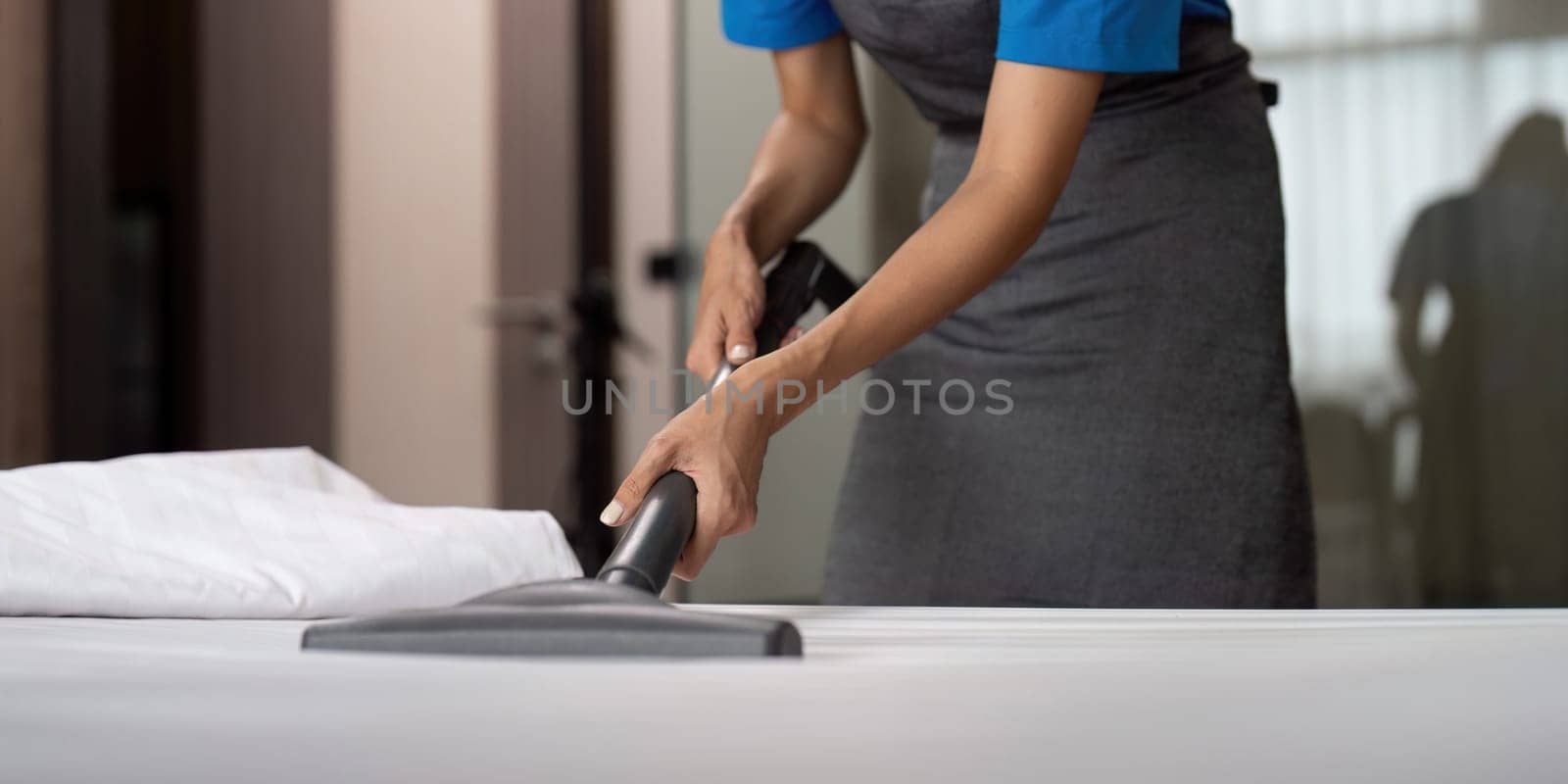 Cleaning service employee removing dirt from with professional equipment. Female housekeeper cleaning the mattress on the bed with vacuum cleaner.